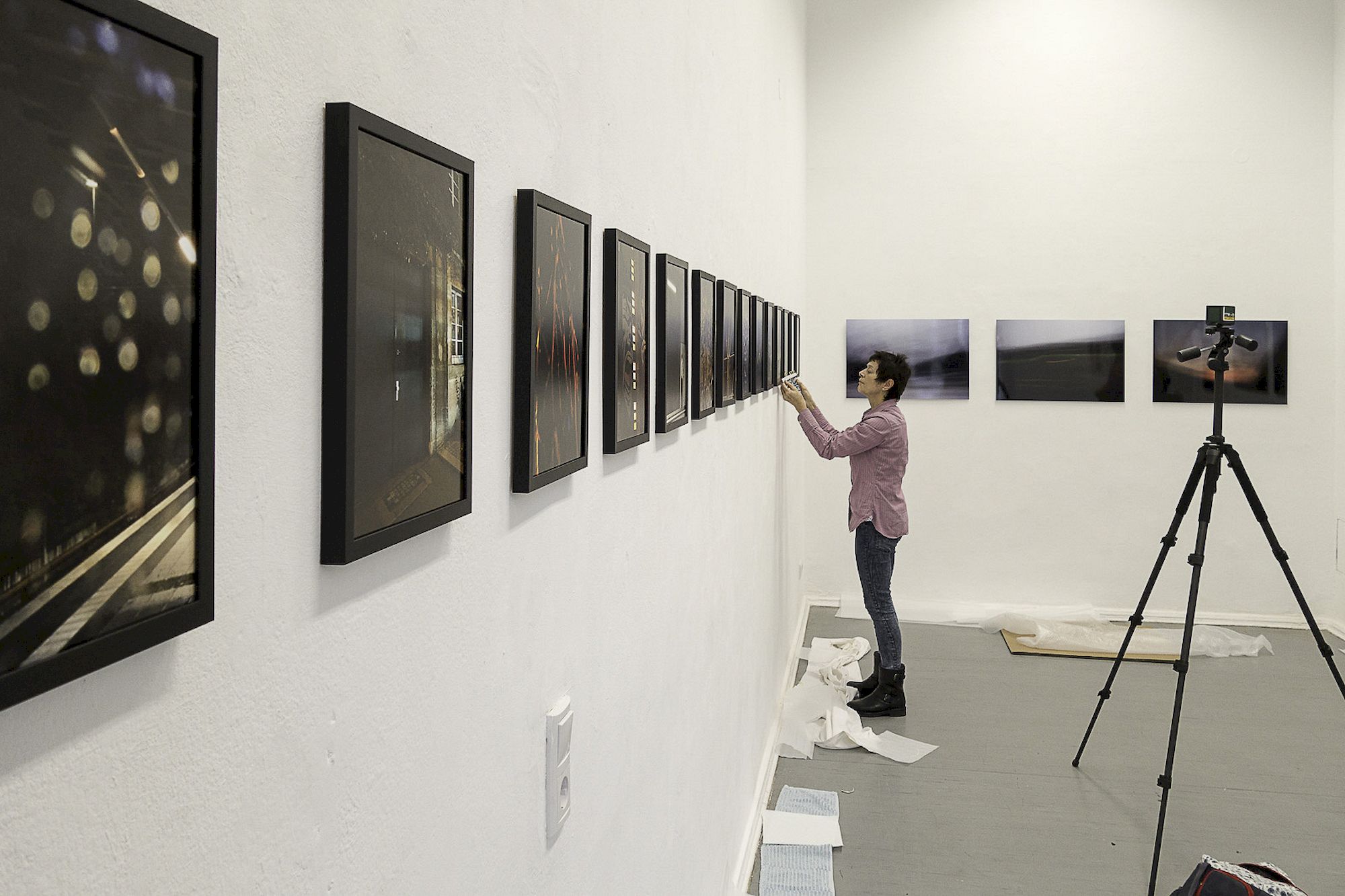 Eine Frau arbeitet daran, Bilder für eine Ausstellung an einer weißen Wand gerade auszurichten.