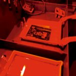 Eine Person arbeitet bei rotem licht in einer Dunkelkammer. In einer Schale mit Flüssigkeit liegt ein Schwarzweiß-Bild.