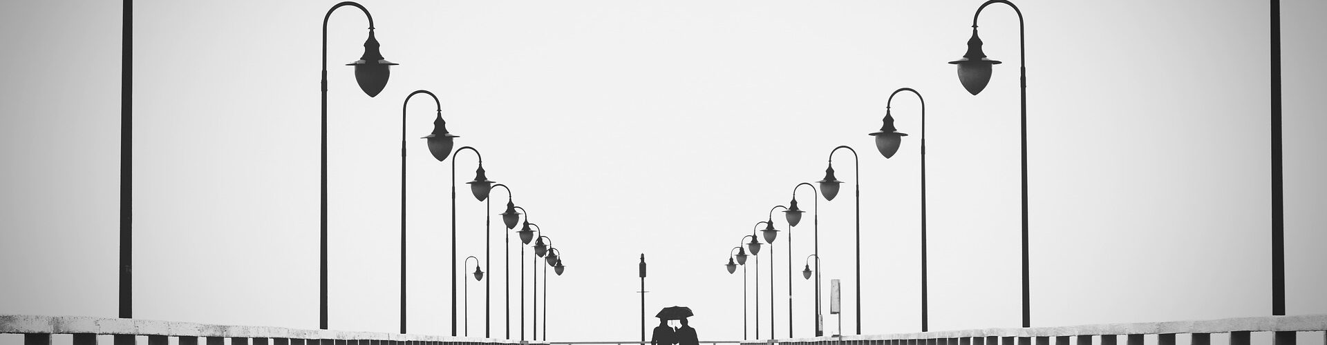 Ein Schwarz-Weiß-Foto eines Paares, das auf einem Pier läuft. Das Bild lebt von der Symmetrie.