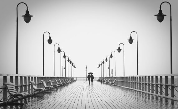 Ein Schwarz-Weiß-Foto eines Paares, das auf einem Pier läuft. Das Bild lebt von der Symmetrie.