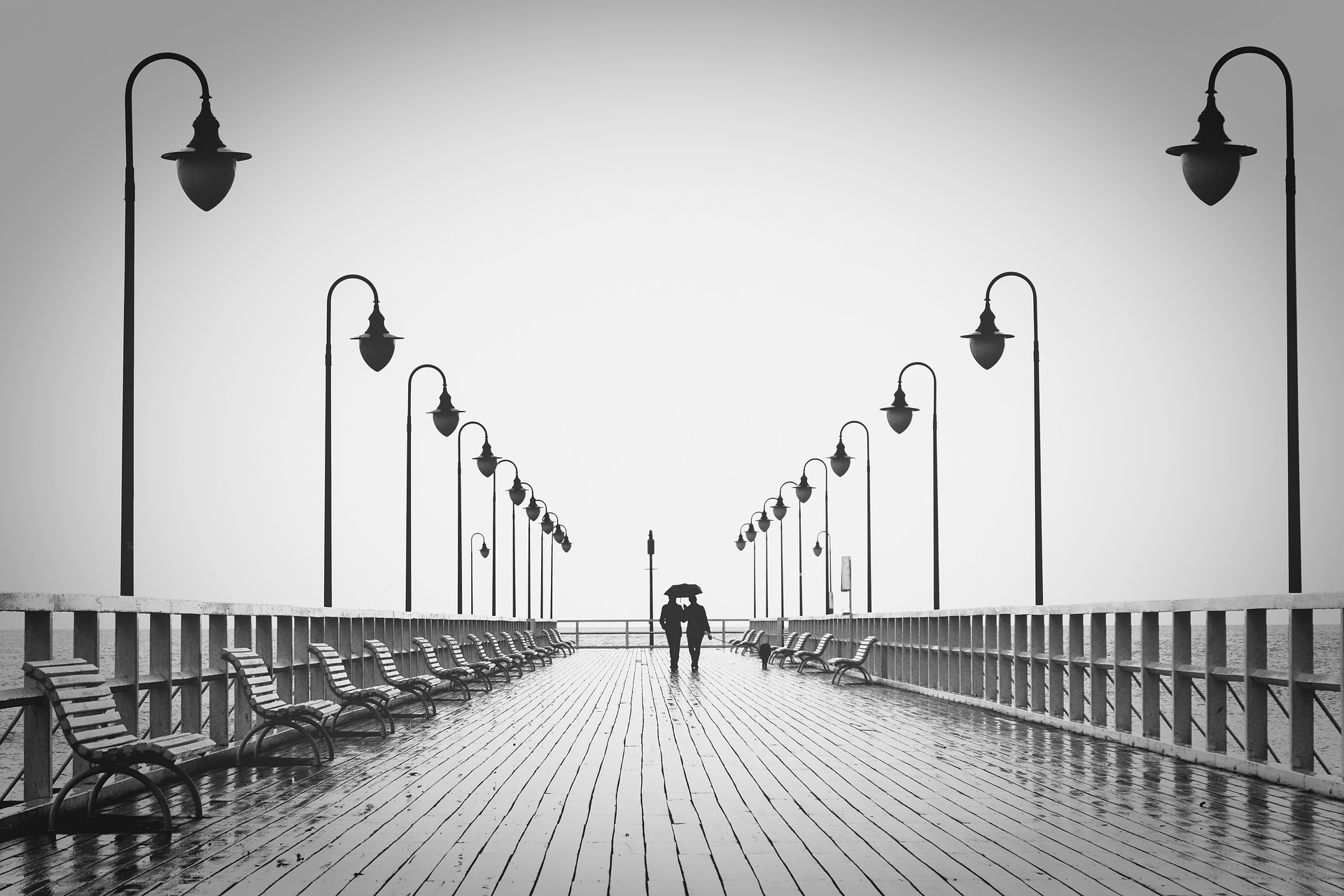 Ein Schwarz-Weiß-Foto eines Paares, das auf einem Pier läuft. Das Bild lebt von der Symmetrie.