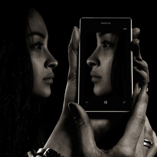 Ein Schwarz-Weiß-Foto einer Frau, die sich in einem Mobiltelefon spiegelt.