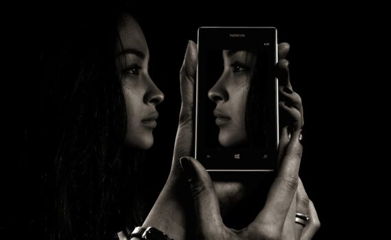 Ein Schwarz-Weiß-Foto einer Frau, die sich in einem Mobiltelefon spiegelt.