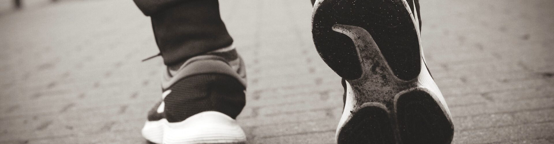 Die Turnschuhe einer Person, die einen gemauerten Gehweg hinuntergeht.