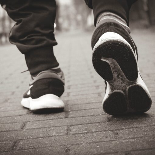 Die Turnschuhe einer Person, die einen gemauerten Gehweg hinuntergeht.