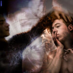 Ein digital bearbeitetes Bild eines nachdenklichen Mannes mit überlappenden, abstrakten Elementen und verschwommenen Gesichtern in einer stimmungsvollen, künstlerischen Komposition. (KI generierte Beschreibung)