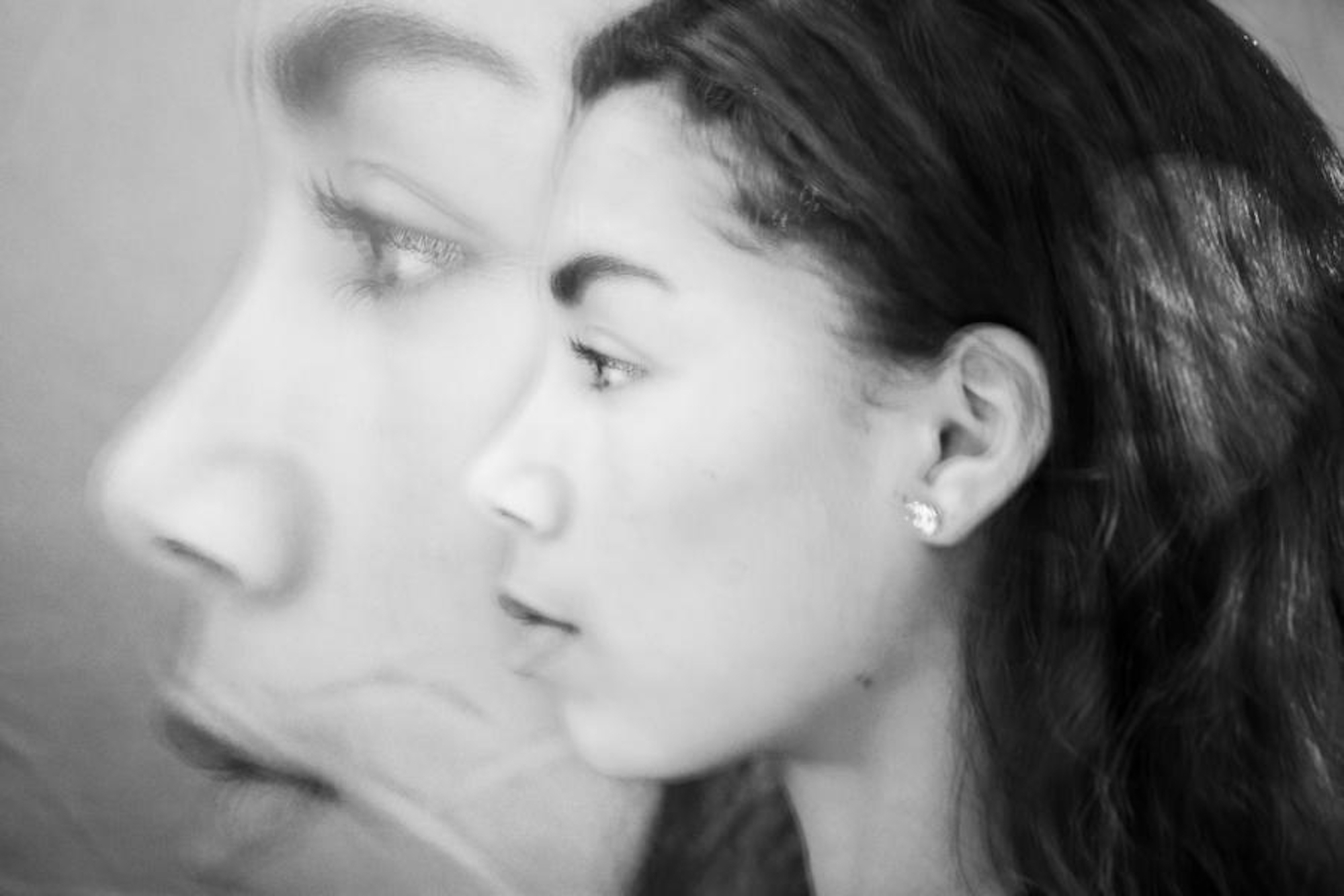 Ein Schwarz-Weiß-Foto zeigt eine Frau im Profil, deren Gesicht von einem größeren, halbtransparenten Seitenprofil ihres eigenen Gesichts überlagert wird. (KI generierte Beschreibung)