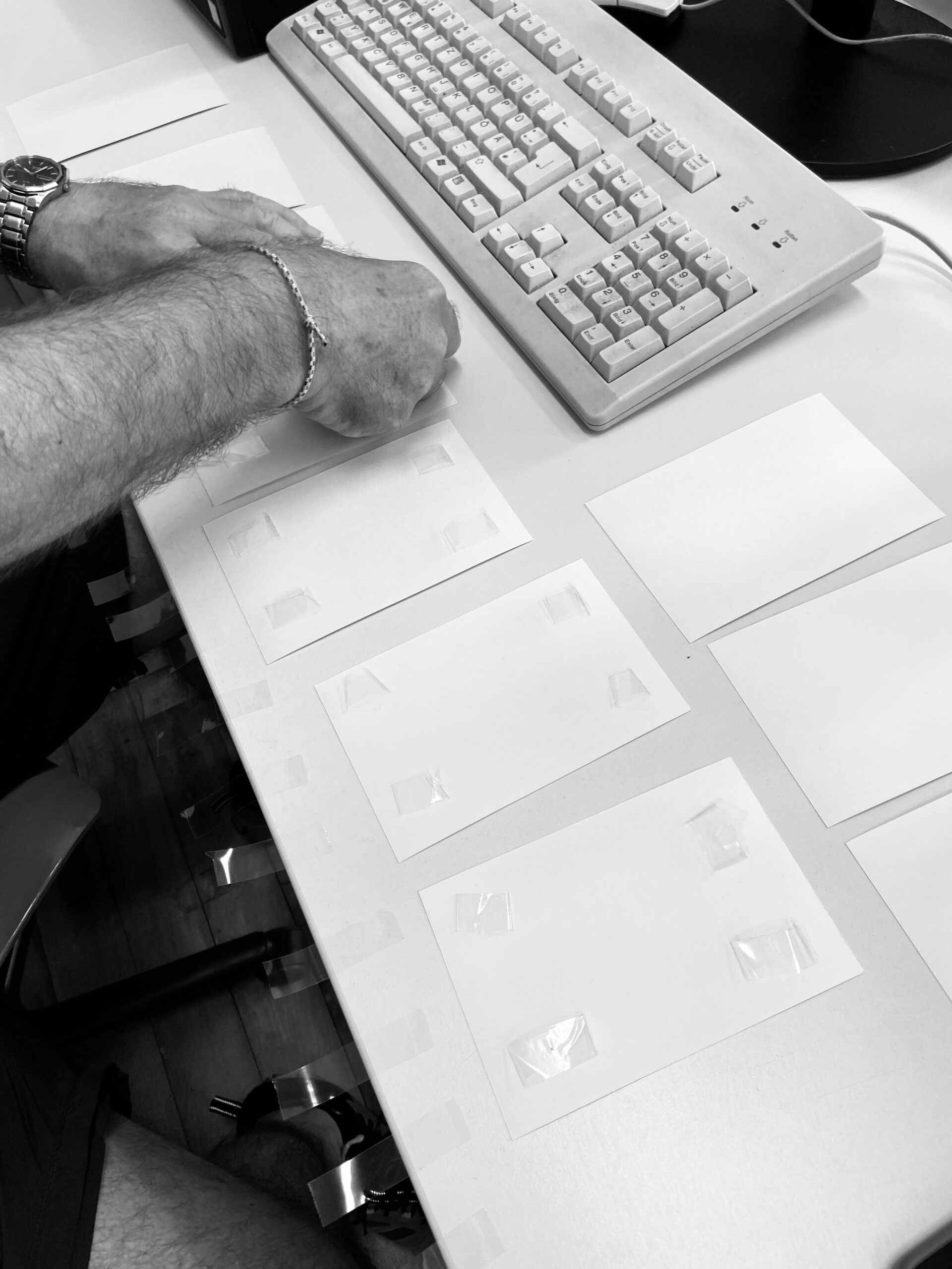 Eine Person ordnet mit Klebeband befestigte Blätter Papier auf einem Schreibtisch neben einer Tastatur an. (KI generierte Beschreibung)