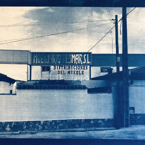 Ein altes Foto eines Möbelvertriebsgebäudes mit Schildern mit der Aufschrift „Distribuciones del Mueble“ und teilweiser Sichtbarkeit von „Muebles y Muebles S.L.“, umgeben von einer niedrigen Mauer. (KI generierte Beschreibung)