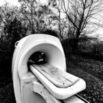 Verlassenes MRT-Gerät im Freien, umgeben von kahlen Bäumen in Schwarz und Weiß. (KI generierte Beschreibung)