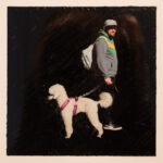 Eine Person in Jacke und Mütze läuft mit einem weißen Pudel an einer rosa Leine vor einem dunklen Hintergrund. (KI generierte Beschreibung)