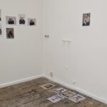 In einem kleinen Galerieraum sind Porträtfotografien an den Wänden und mehrere Drucke auf einem abgenutzten Holzboden ausgestellt. (KI generierte Beschreibung)