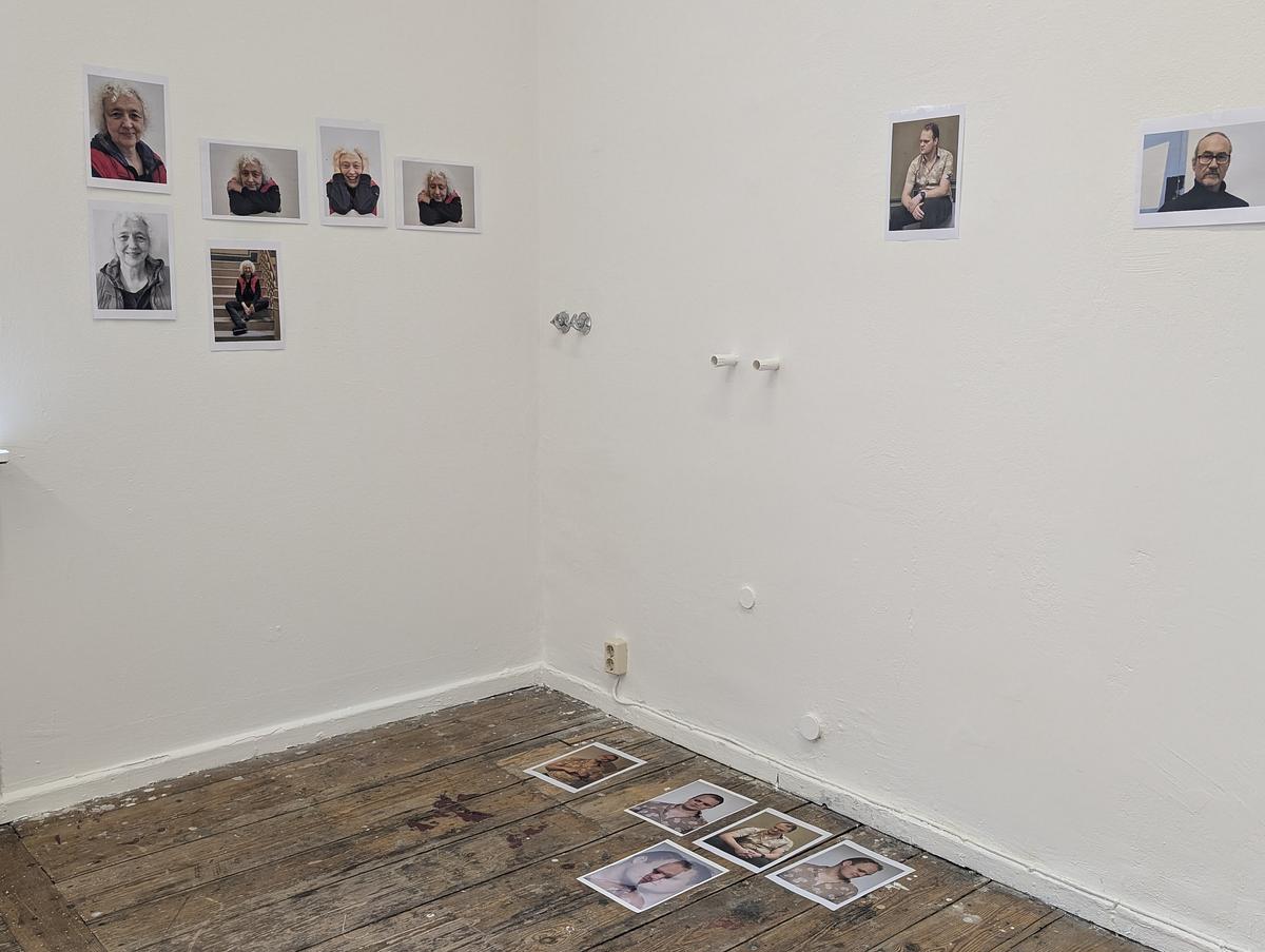 In einem kleinen Galerieraum sind Porträtfotografien an den Wänden und mehrere Drucke auf einem abgenutzten Holzboden ausgestellt. (KI generierte Beschreibung)