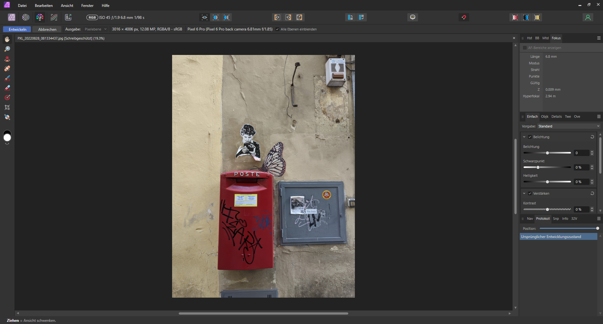 Fenster einer Bildbearbeitungssoftware mit einem Bild eines roten Briefkastens mit Graffiti, einer schwarz-weißen Kinderskulptur und Schmetterlingsflügeln an einer Wand. (KI generierte Beschreibung)