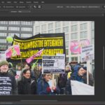 Eine Gruppe von Demonstranten, die bei einer Demonstration Schilder und Transparente mit deutschem Text auf den Schildern halten, in einer städtischen Außenanlage. (KI generierte Beschreibung)