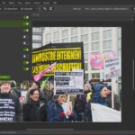 Das Fenster einer Fotobearbeitungssoftware zeigt ein Bild eines Straßenprotests mit Menschen, die Schilder und Transparente in deutscher Sprache halten. Auf dem Bildschirm sind Bearbeitungswerkzeuge und Einstellungsfelder zu sehen. (KI generierte Beschreibung)