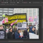 Das Fenster einer Fotobearbeitungssoftware zeigt ein Bild eines Straßenprotests mit Menschen, die Transparente und Schilder in deutscher Sprache halten, vor dem Hintergrund moderner Gebäude. (KI generierte Beschreibung)