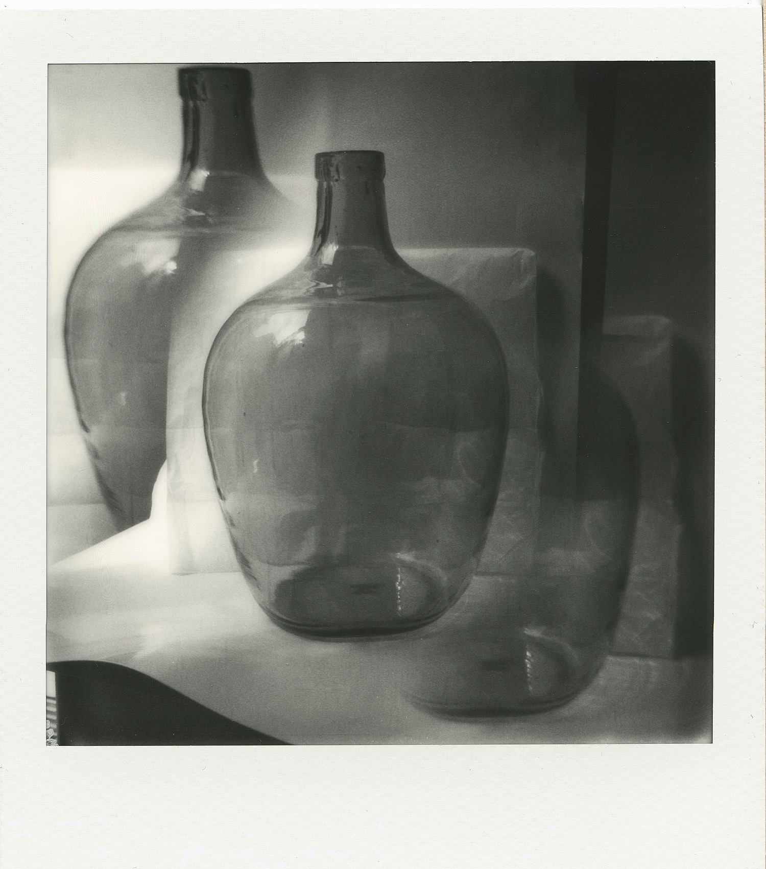 Ein Schwarz-Weiß-Foto von drei durchsichtigen Glasflaschen, auf denen Licht und Schatten sich überlagernde Reflexionen erzeugen. (KI generierte Beschreibung)