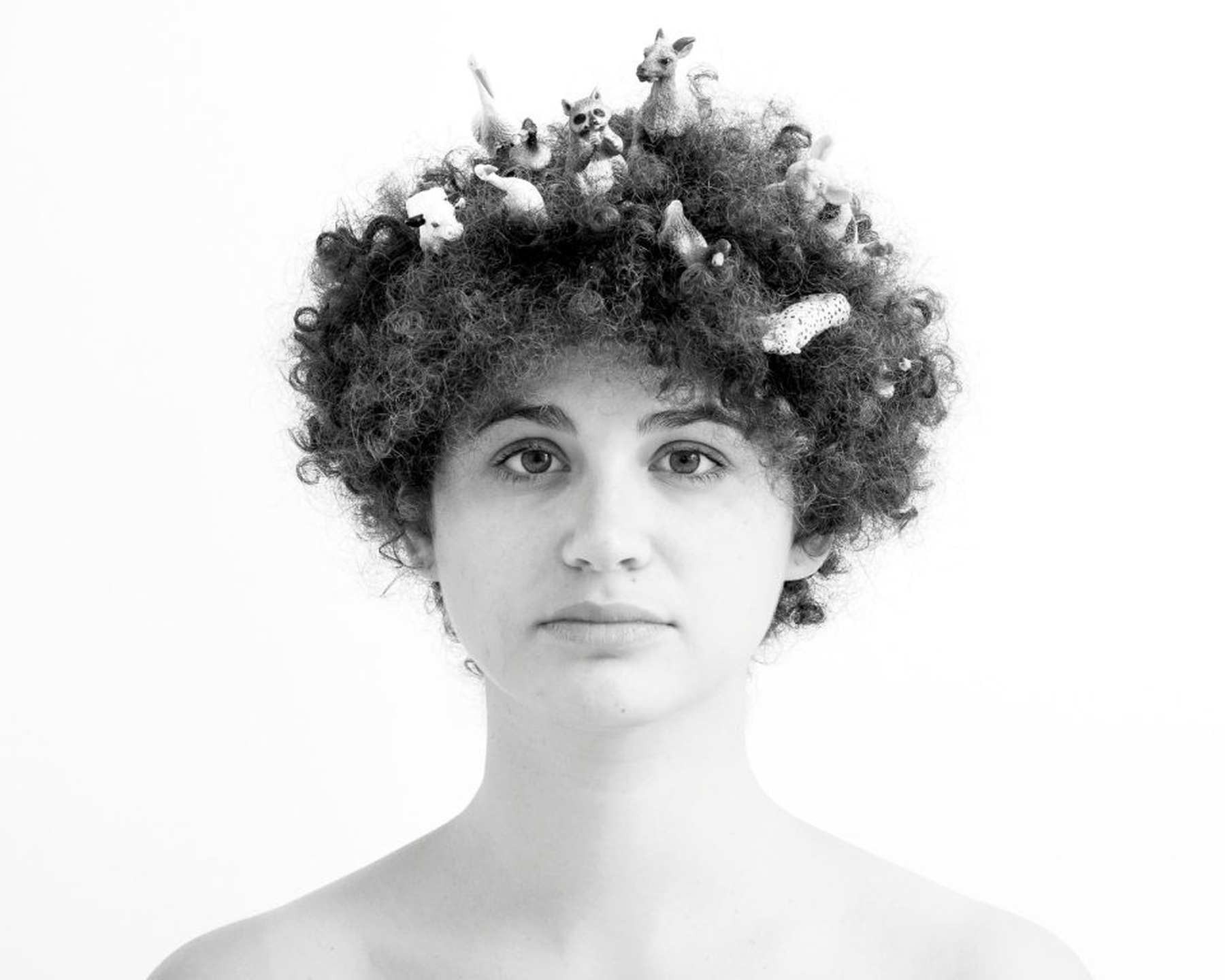 Eine Person mit lockigem Haar, in dessen Locken kleine Tierfiguren eingebettet sind. (KI generierte Beschreibung)
