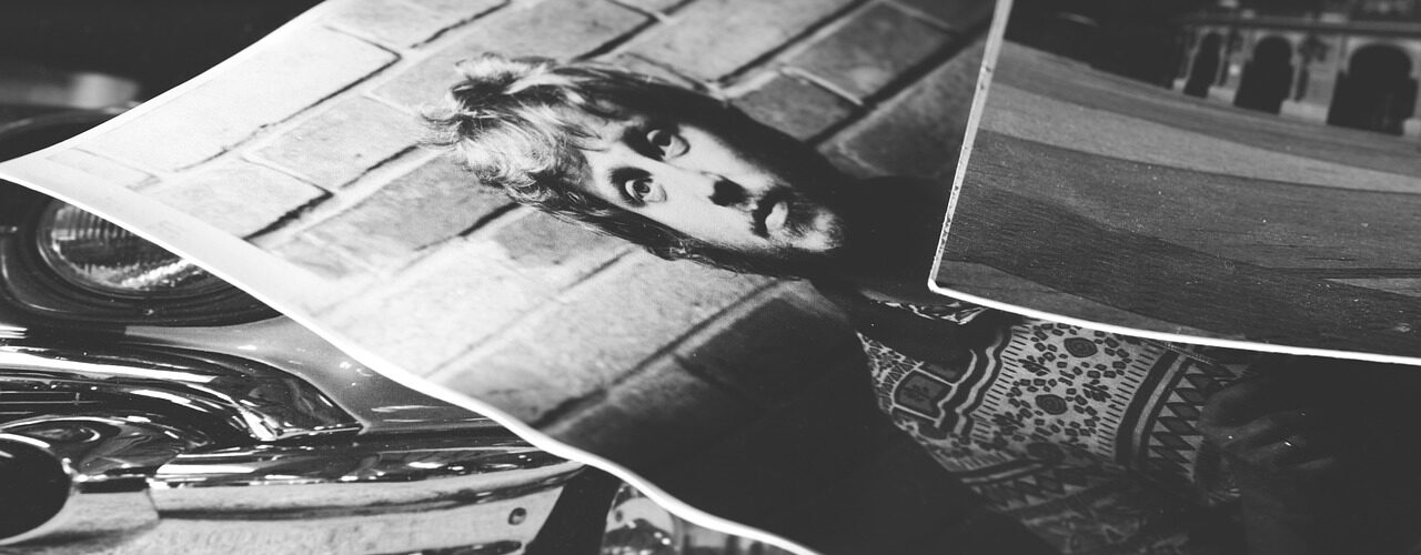 Schwarz-Weiß-Fotodrucke, die sich überlagern: einer zeigt eine Person vor einer Backsteinmauer, ein anderer einen Teil eines Oldtimers und ein dritter ein Gebäude im Hintergrund. (KI generierte Beschreibung)