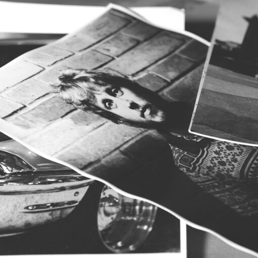 Schwarz-Weiß-Fotodrucke, die sich überlagern: einer zeigt eine Person vor einer Backsteinmauer, ein anderer einen Teil eines Oldtimers und ein dritter ein Gebäude im Hintergrund. (KI generierte Beschreibung)