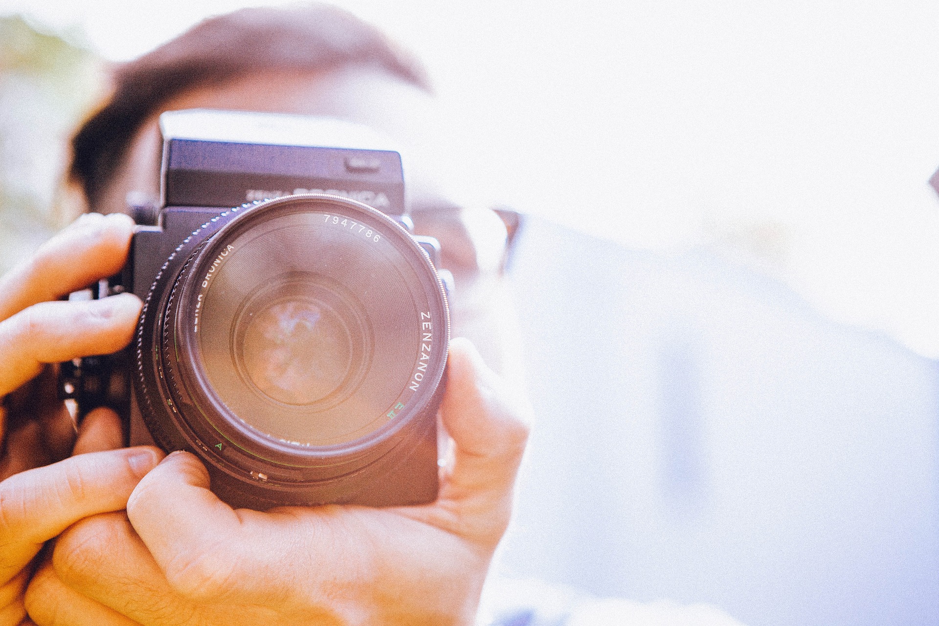 Person, die eine Zenza-Bronica-Kamera nahe an ihr Gesicht hält, um ein Foto zu machen, mit hellem Sonnenlicht im Hintergrund. (KI generierte Beschreibung)