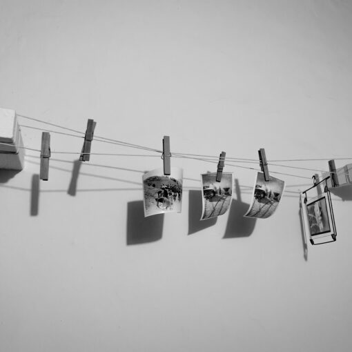 Schwarzweißfoto von mehreren Bildern, die an einer Schnur an einer weißen Wand befestigt sind und einer Wäscheleine ähneln. (KI generierte Beschreibung)