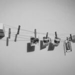 Vier kleine Fotos hängen an einer Schnur mit Wäscheklammern, die an zwei Schaumstoffblöcken an einer weißen Wand befestigt sind. Das Bild ist in schwarz-weiß gehalten. (KI generierte Beschreibung)