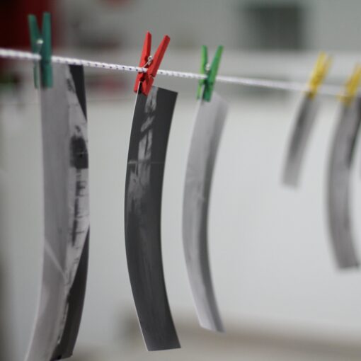 Schwarzweißfotos hängen an einer Leine mit bunten Wäscheklammern vor unscharfem Hintergrund. (KI generierte Beschreibung)