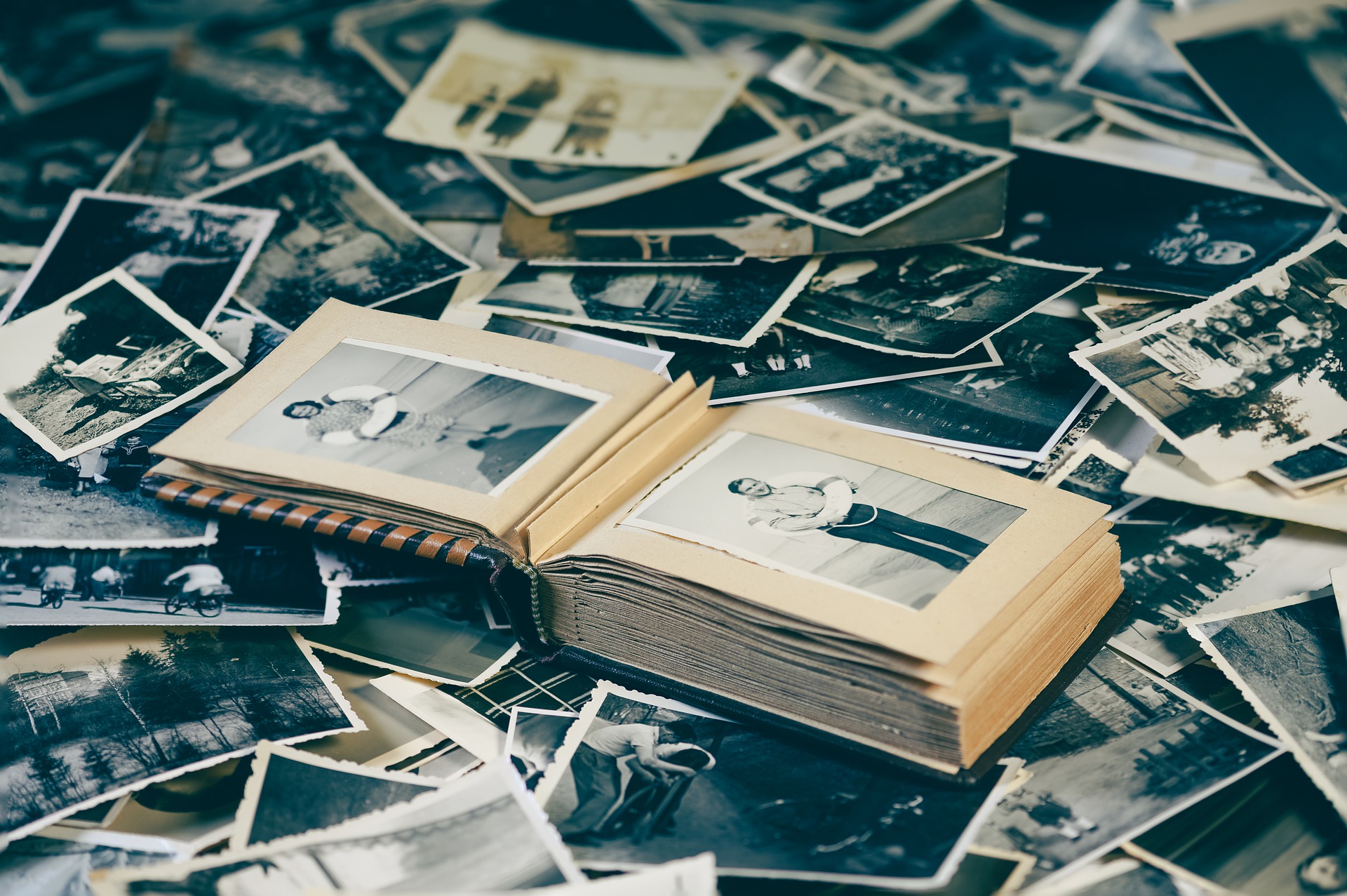 Ein offenes Fotoalbum mit Schwarzweißbildern, umgeben von verstreuten Vintage-Fotografien. (KI generierte Beschreibung)