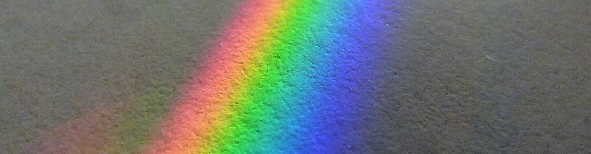 Ein Spektrum heller Farben, die auf einer strukturierten grauen Oberfläche einen Regenbogen bilden. (KI generierte Beschreibung)