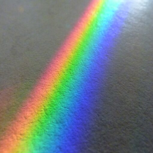 Ein Spektrum heller Farben, die auf einer strukturierten grauen Oberfläche einen Regenbogen bilden. (KI generierte Beschreibung)