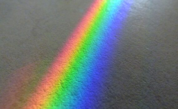 Ein Spektrum heller Farben, die auf einer strukturierten grauen Oberfläche einen Regenbogen bilden. (KI generierte Beschreibung)
