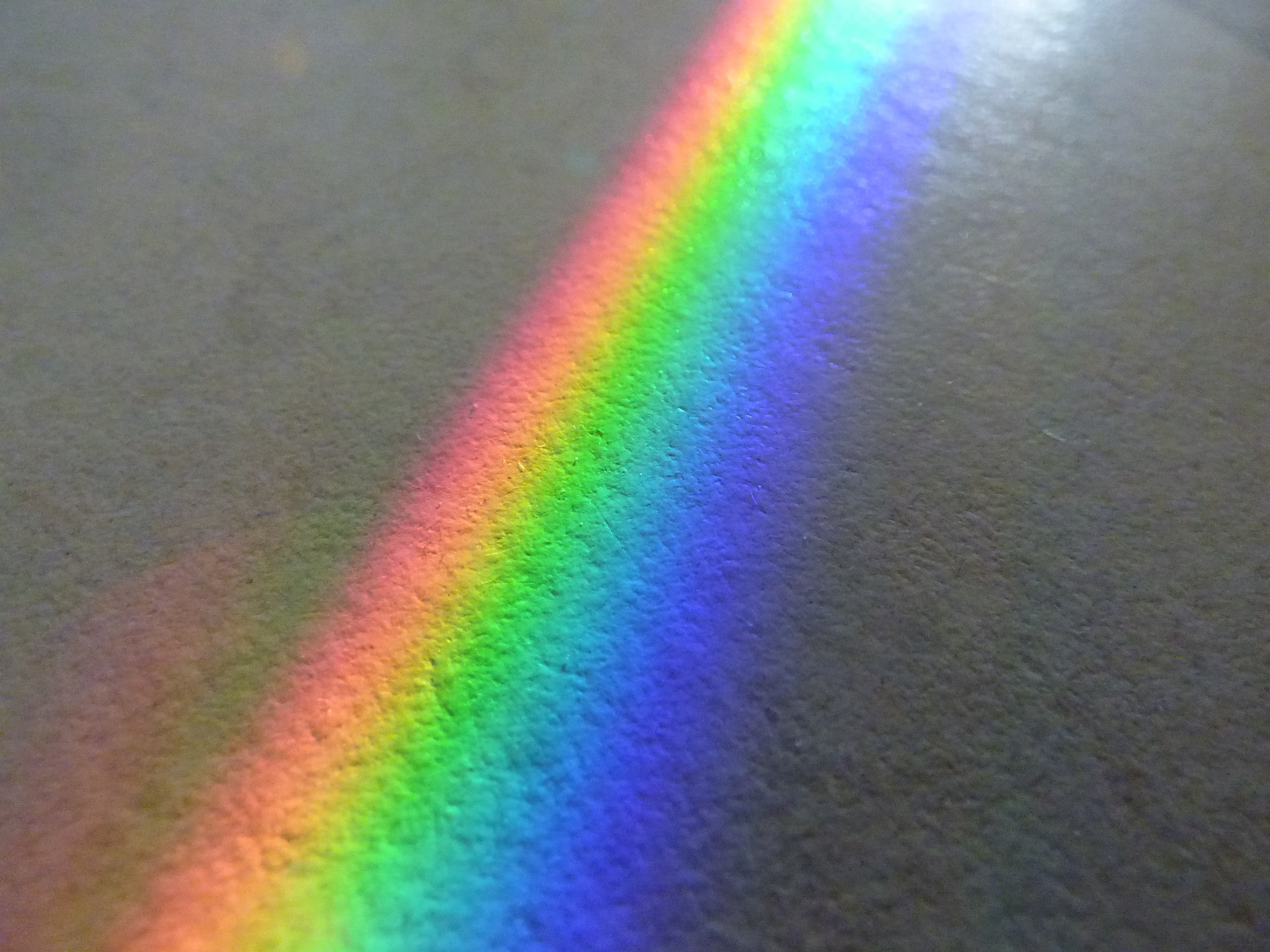 Ein Spektrum heller Farben, die auf einer strukturierten grauen Oberfläche einen Regenbogen bilden. (KI generierte Beschreibung)