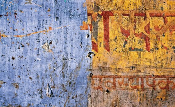 Verwitterte Wand mit verblasster blauer Farbe auf der linken Seite und gelber Farbe mit roter und orangefarbener Schrift auf der rechten Seite. (KI generierte Beschreibung)