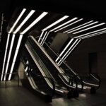 Moderne Rolltreppen mit beleuchteten Deckenleuchten in einem schwach beleuchteten Innenraum. (KI generierte Beschreibung)