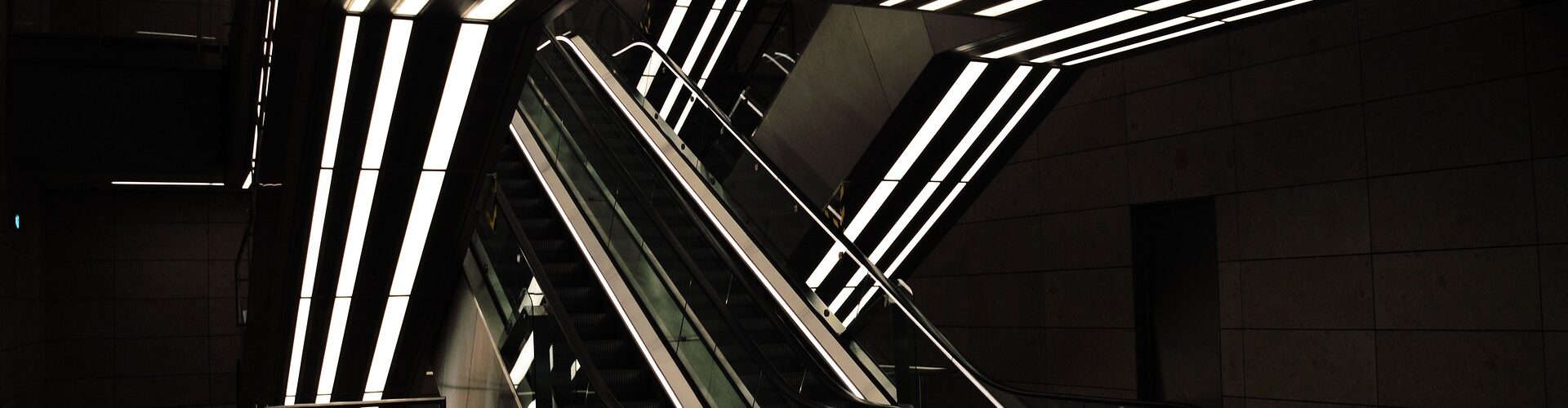 Moderne Rolltreppen mit beleuchteten Deckenleuchten in einem schwach beleuchteten Innenraum. (KI generierte Beschreibung)