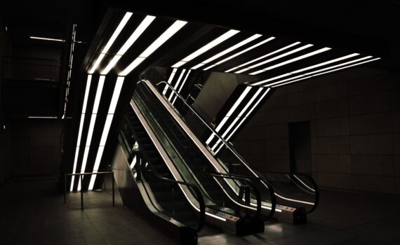 Moderne Rolltreppen mit beleuchteten Deckenleuchten in einem schwach beleuchteten Innenraum. (KI generierte Beschreibung)