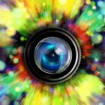 Eine Kameralinse steht in der Mitte eines lebhaften, farbenfrohen Lichtblitzes und eines Bokehs, wodurch ein Effekt entsteht, der an ein Auge erinnert. (KI generierte Beschreibung)