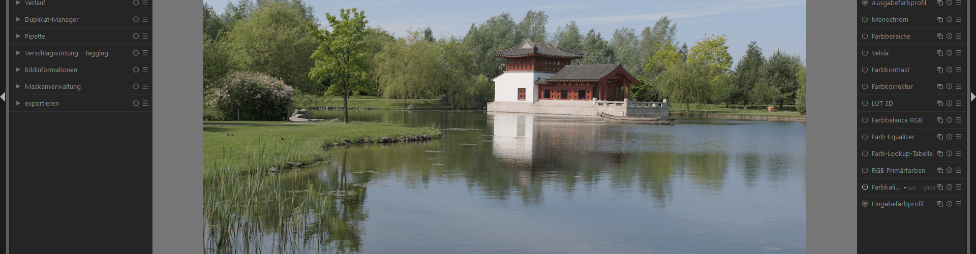 Ein Pavillon im traditionellen Stil steht an einem spiegelnden Teich, der von Bäumen umgeben ist, mit blauem Himmel und Wolkenfetzen über dem Kopf, dargestellt in einer Fotobearbeitungssoftware. (KI generierte Beschreibung)