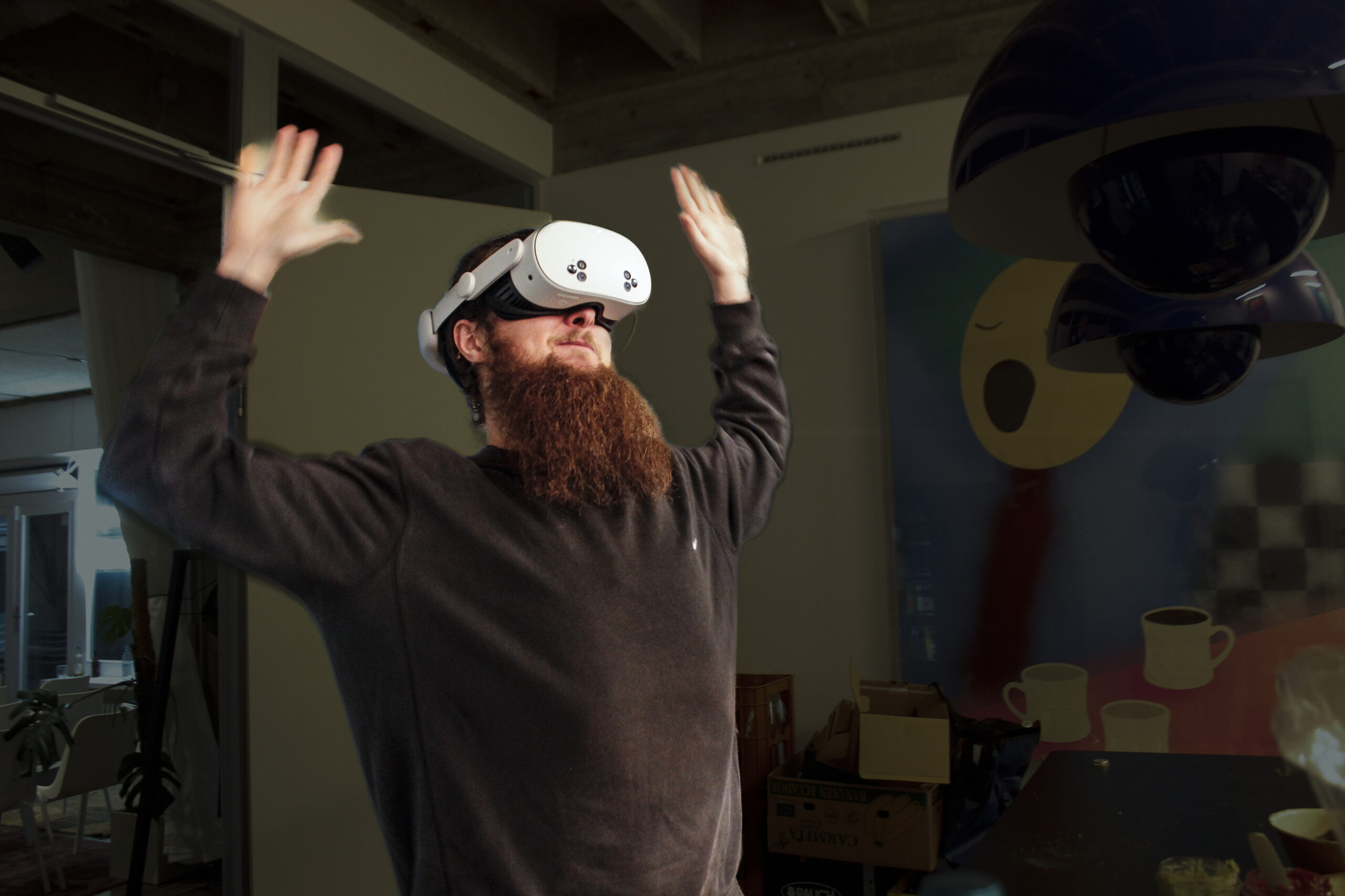 Eine bärtige Person, die ein Virtual-Reality-Headset trägt, steht mit erhobenen Armen in einem Raum mit abstrakter Kunst und verschiedenen Objekten im Hintergrund. (KI generierte Beschreibung)