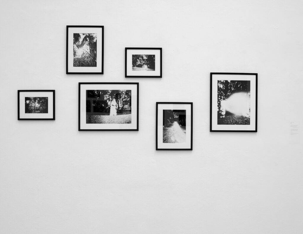 Sechs Schwarz-Weiß-Fotografien in schwarzen Rahmen sind versetzt an einer schlichten weißen Wand angeordnet. (KI generierte Beschreibung)