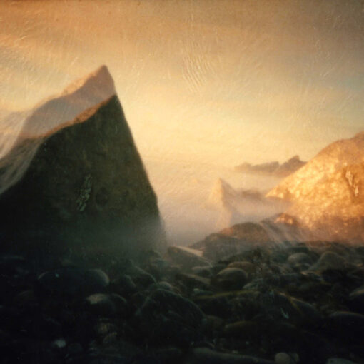 Große Felsen und Kieselsteine am Ufer werden von warmem, sanftem Sonnenlicht beleuchtet, während Nebel oder Dunst eine traumhafte, ätherische Atmosphäre schaffen. (KI generierte Beschreibung)