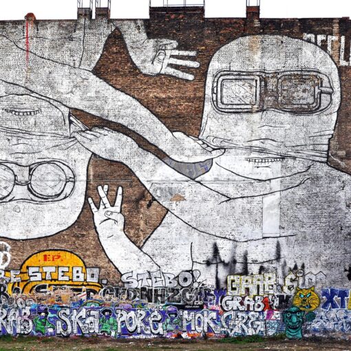 Große Wandtapete mit zwei Comicfiguren mit Schutzbrillen, von denen eine aufrecht und die andere auf dem Kopf steht, vor einer Backsteinmauer, die im unteren Bereich mit bunten Graffiti-Tags übersät ist. (KI generierte Beschreibung)