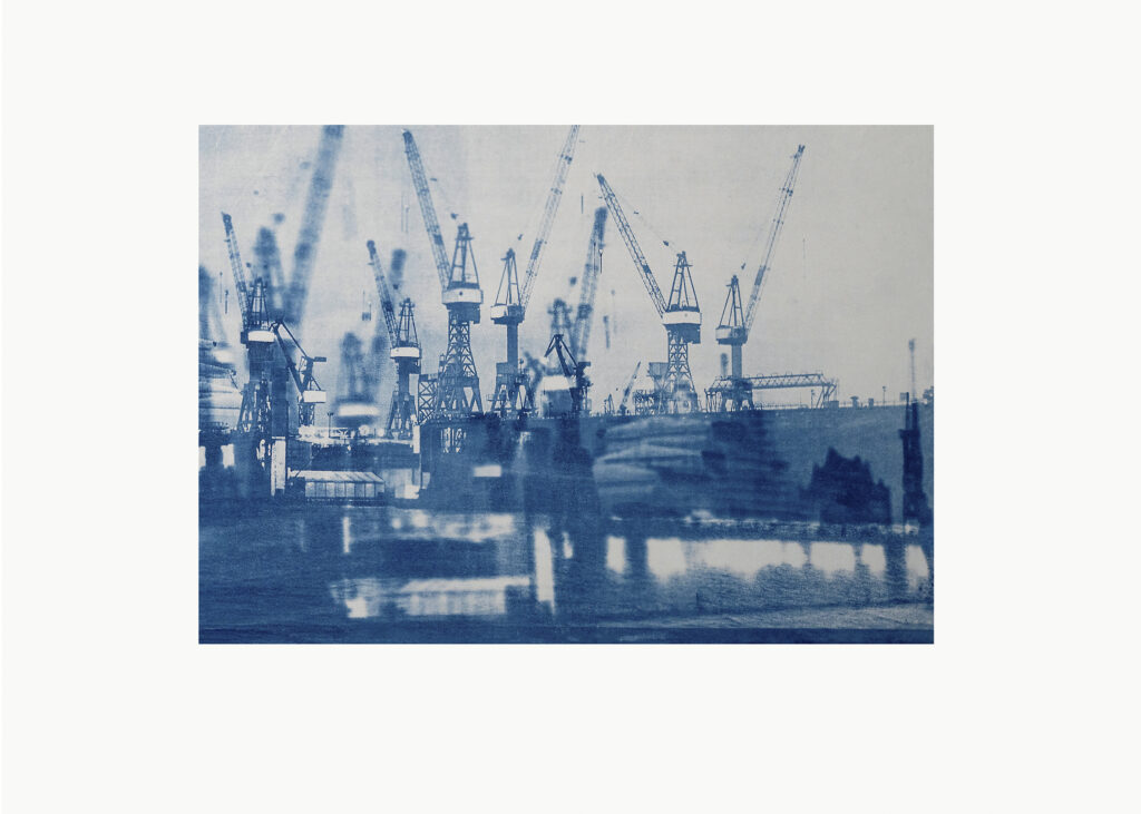 Monochromes, in Blautönen gehaltenes Bild mehrerer Kräne in einem Industriehafen, auf dem sich im Wasser darunter Spiegelungen erkennen lassen. (KI generierte Beschreibung)