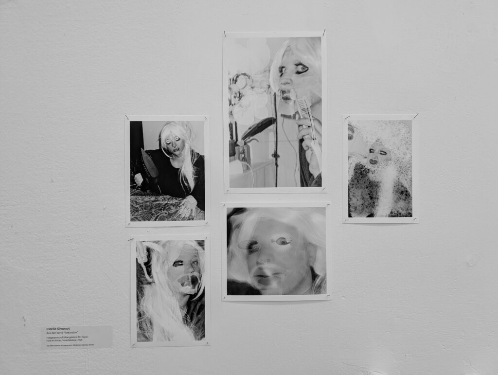 Fünf monochrome, verzerrte Fotoporträts einer Person mit langen Haaren sind in einer Gruppe an einer weißen Wand ausgestellt. (KI generierte Beschreibung)