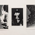 An einer weißen Wand sind drei abstrakte Schwarz-Weiß-Drucke angebracht, die kontrastreiche Formen und Muster zeigen, die an menschliche Profile und Punktansammlungen erinnern. (KI generierte Beschreibung)
